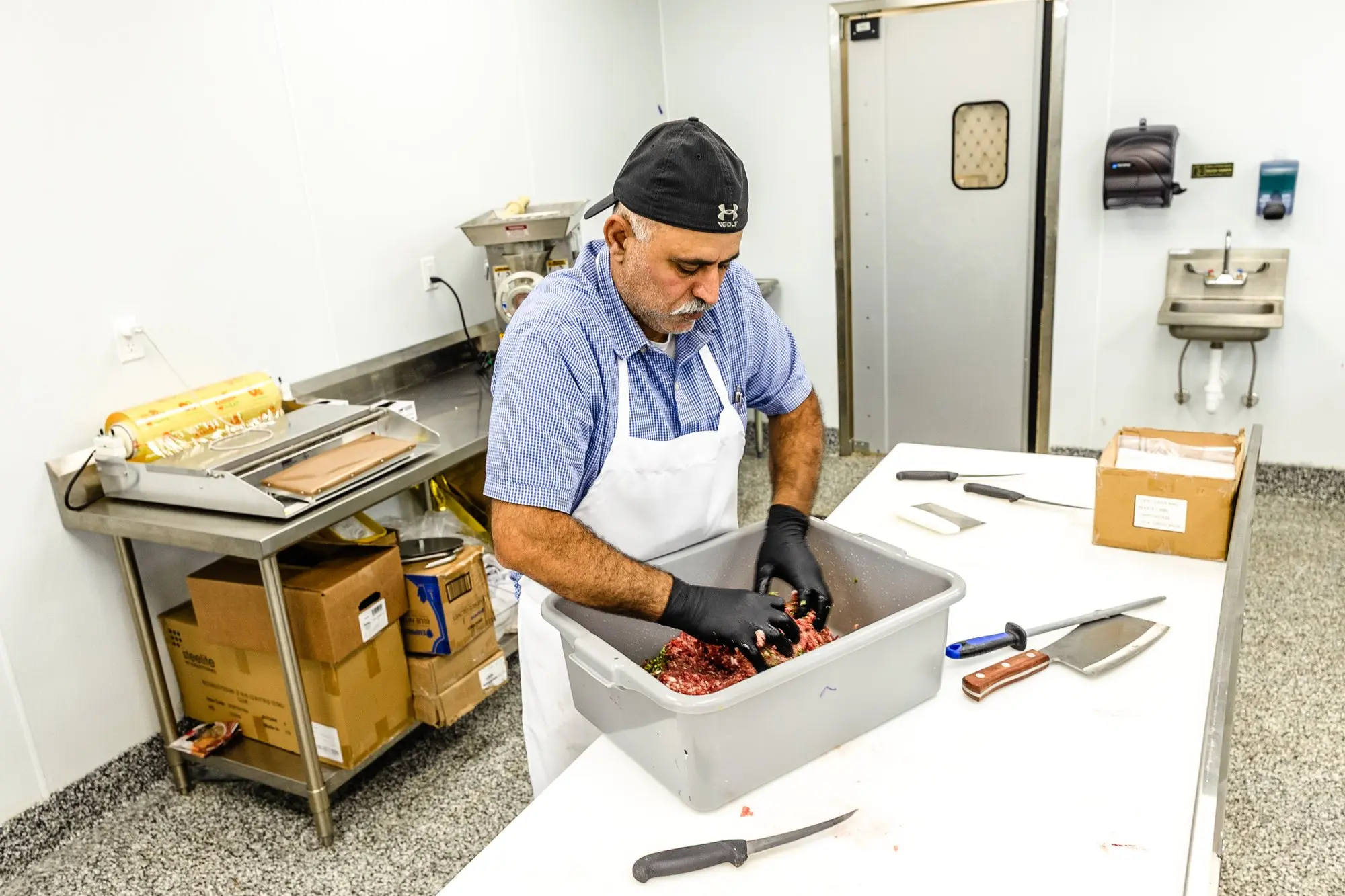 Our butcher, gloved, preparing fresh meat at the counter.