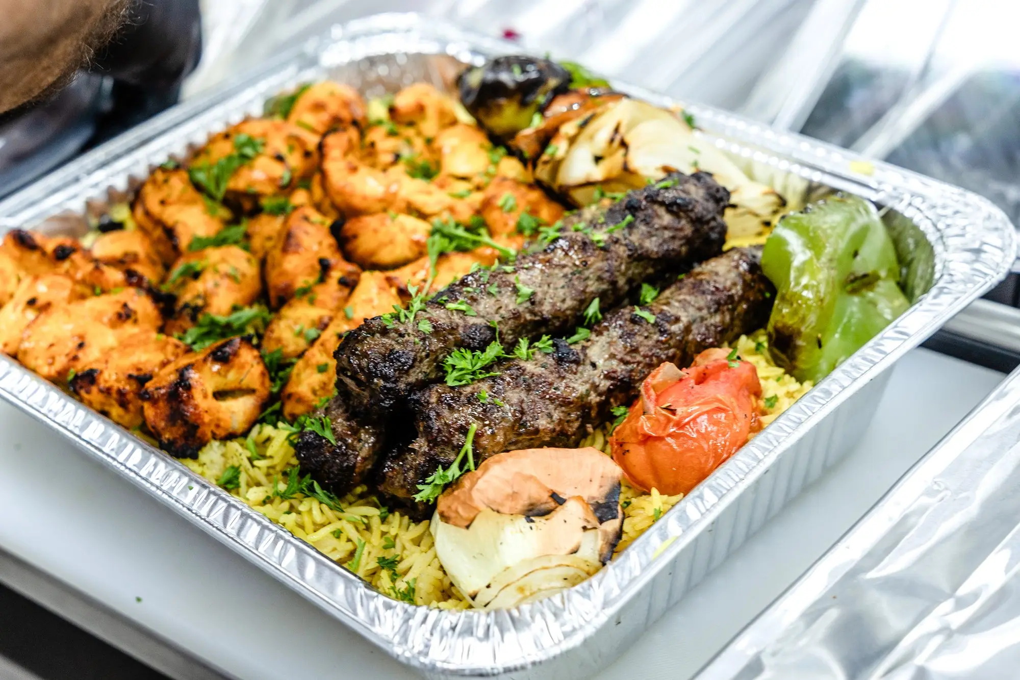 A catering tray of kofta and tawook skewers over rice.