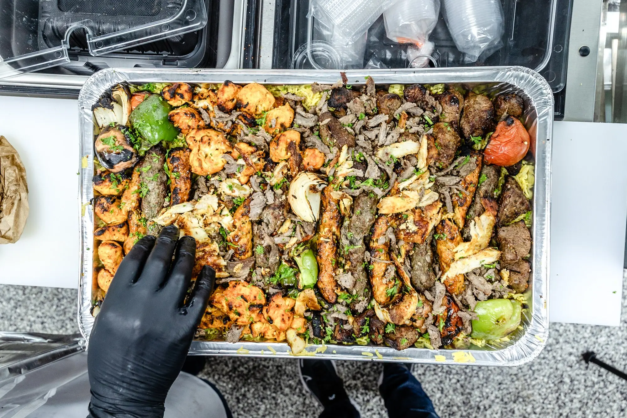 A full mixed grill catering tray held by a gloved hand.