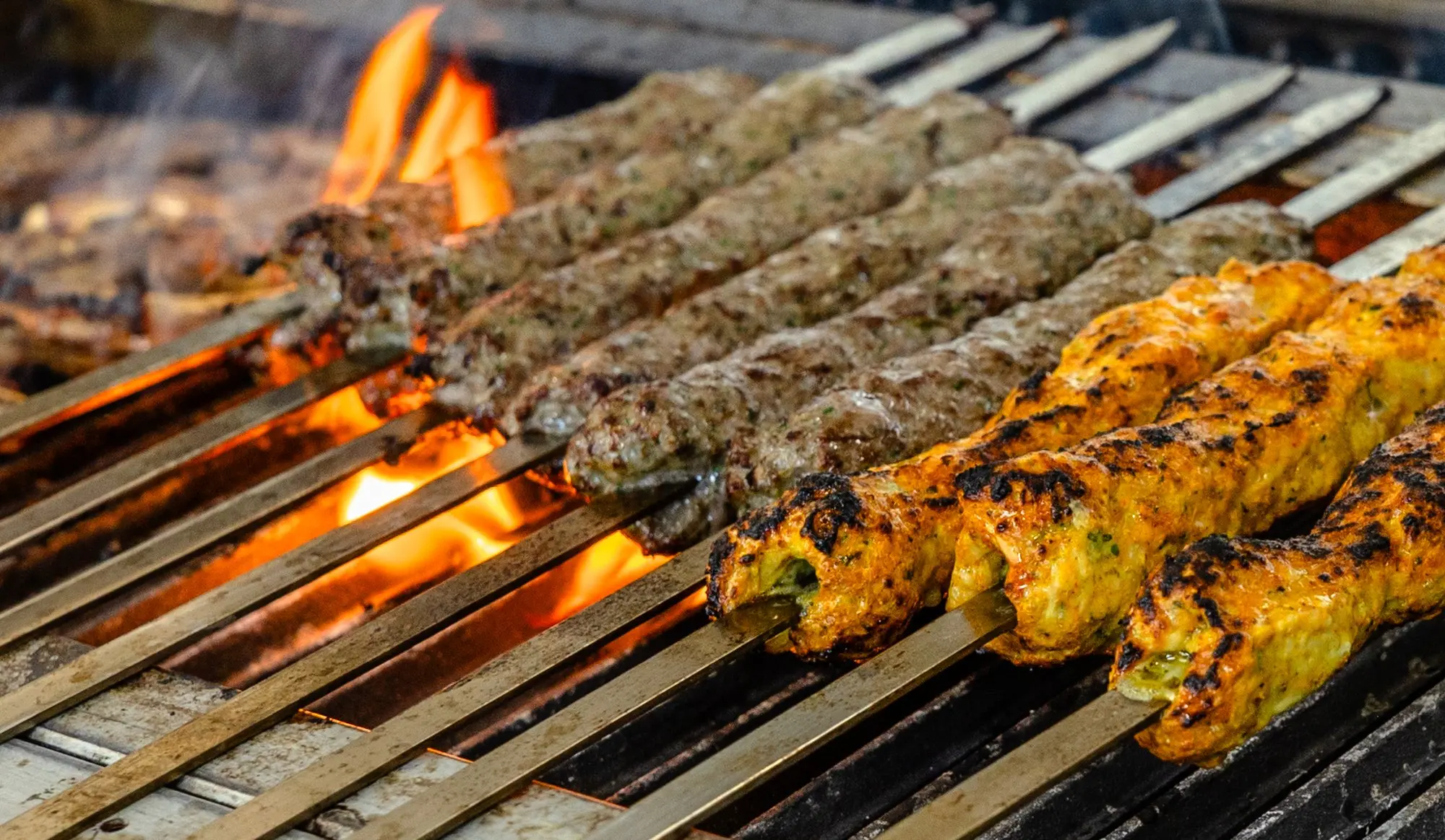 A full grill of beef kofta and chicken tawook skewers over the flame.