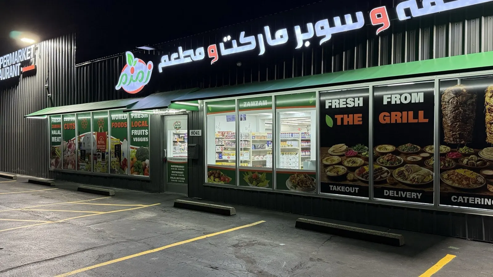 The ZAMZAM storefront at night, its sign and window graphics lit.