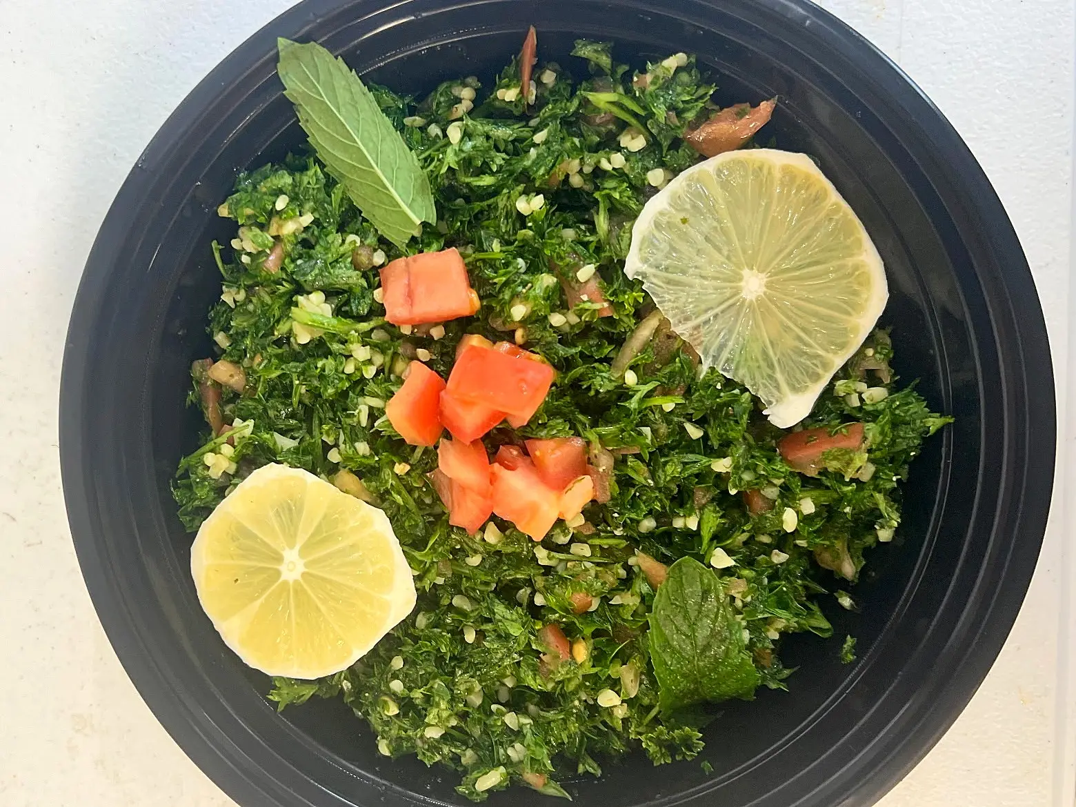 A bowl of tabbouleh: chopped parsley, bulgur and tomato with mint leaves and lemon slices.